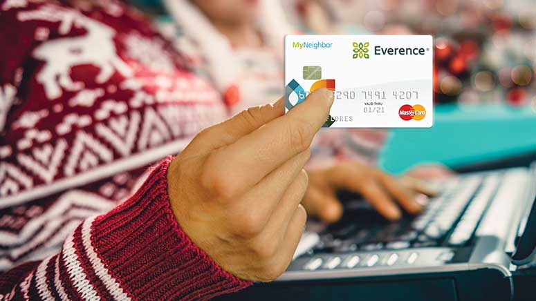 Woman in red Christmas sweater holding laptop holding up MyNeighbor debit card